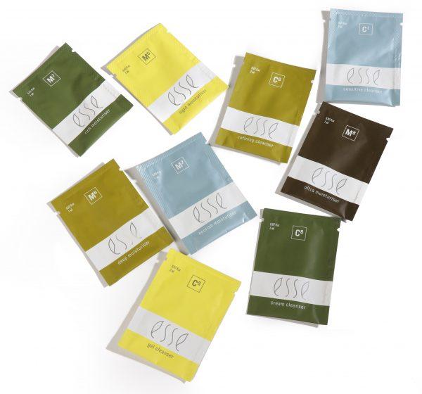Numerous sachets of Esse Samples are scattered across a white background. The packaging features an array of colors, including shades of green, blue, brown, and yellow. Each sachet prominently displays the brand name "Esse" along with specific product details.