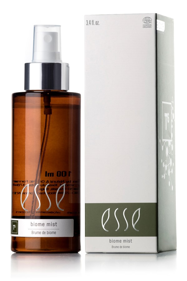 A brown cylindrical spray bottle labeled "Esse Biome Mist" is positioned beside its box packaging. The predominantly white box features green accents at the bottom and displays the same product name. The bottle is equipped with a white spray nozzle and a silver collar.