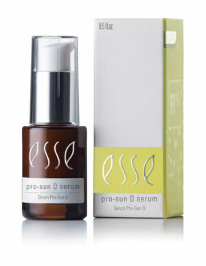 An amber bottle of Esse Pro-Sun D Serum with a white and silver pump standing next to its matching box. The box is predominantly white with green accents, showcasing the same product name along with additional text. The serum bottle contains 0.5 fl. oz.